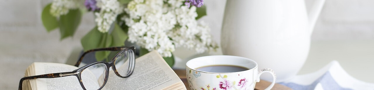 book and reading glasses alongside a cup of tea and a tea pot as relaxation while reading blog posts